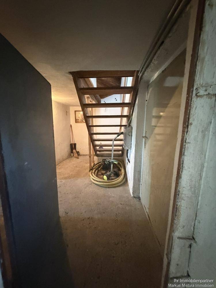 Kellerraum mit Holztreppe und Betonboden, der als Zugang zum Obergeschoss dient.