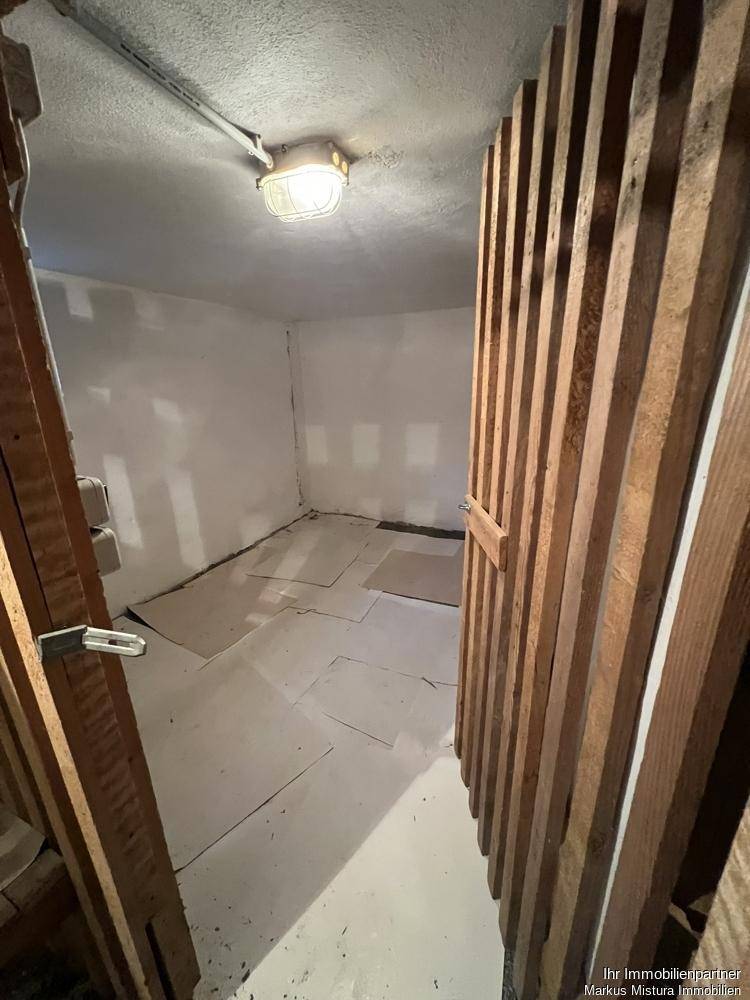 Kleiner, einfacher Kellerraum mit Holzlattenverschlag und Betonboden.