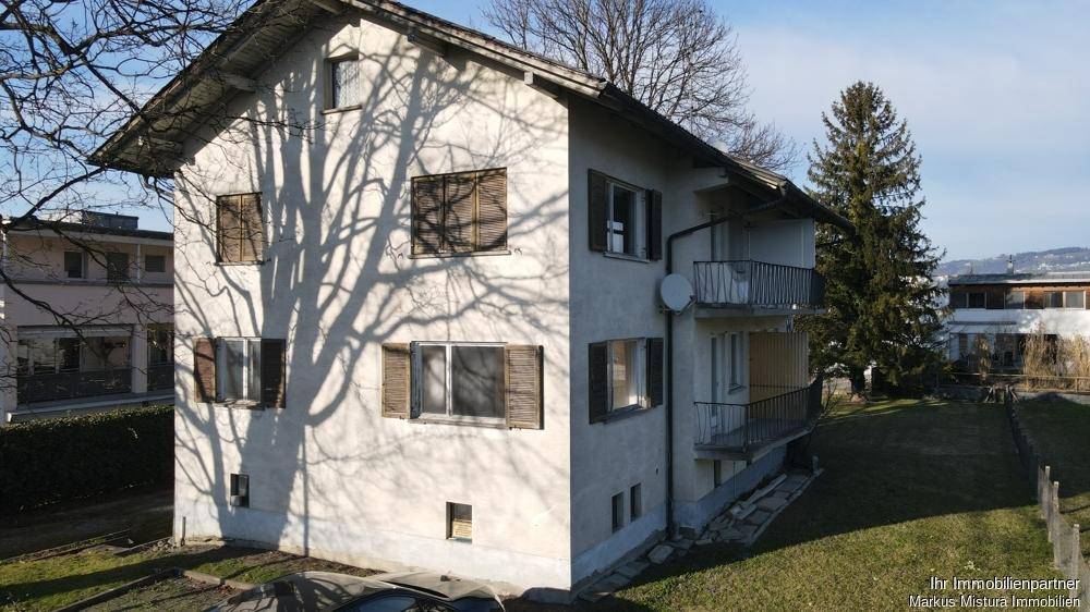Seitenansicht des Gebäudes mit Balkonen, Fensterläden und Schattenwurf von Bäumen.