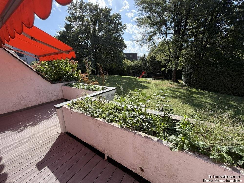 Geräumige Terrasse mit Holzbelag, bepflanzten Hochbeeten und Blick auf den grünen Garten.