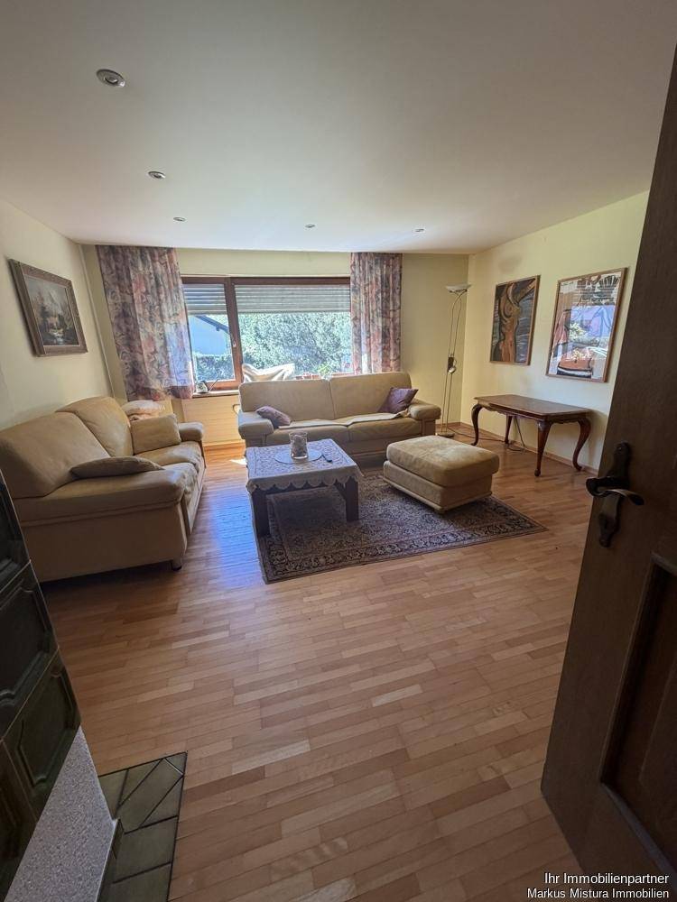 Helles Wohnzimmer mit Parkettboden, beigen Sofas und Blick ins Grüne.