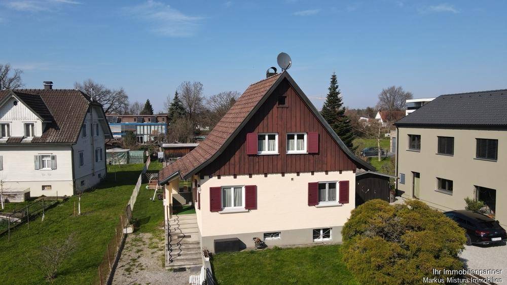 Vogelperspektive eines charmanten Einfamilienhauses mit traditionellem Satteldach und roten Fensterläden.