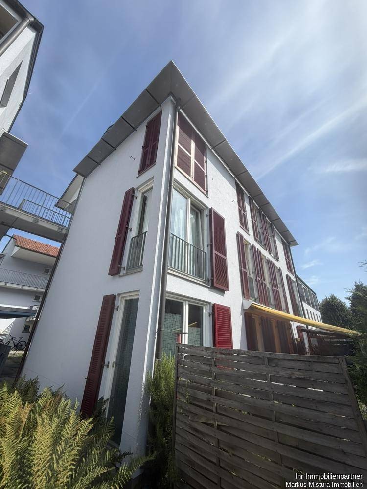 Seitenansicht eines modernen Wohngebäudes mit weißen Fassaden, roten Fensterläden und Balkonen.