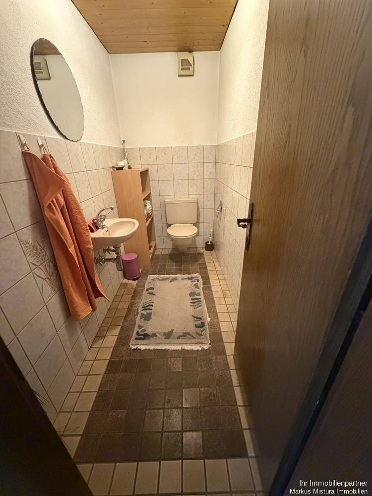 Kleines Gäste-WC mit Fliesenboden und Wandfliesen in hellem Design.