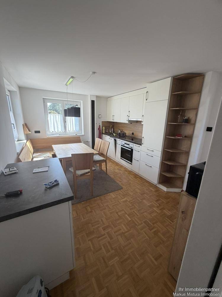Moderne Einbauküche mit weißen Schränken, integrierten Geräten und Essbereich.