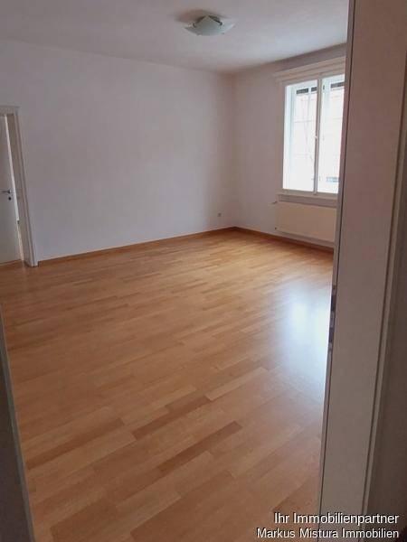Geräumiges Wohnzimmer mit hellem Parkettboden und weiß gestrichenen Wänden, bereit zur Einrichtung.