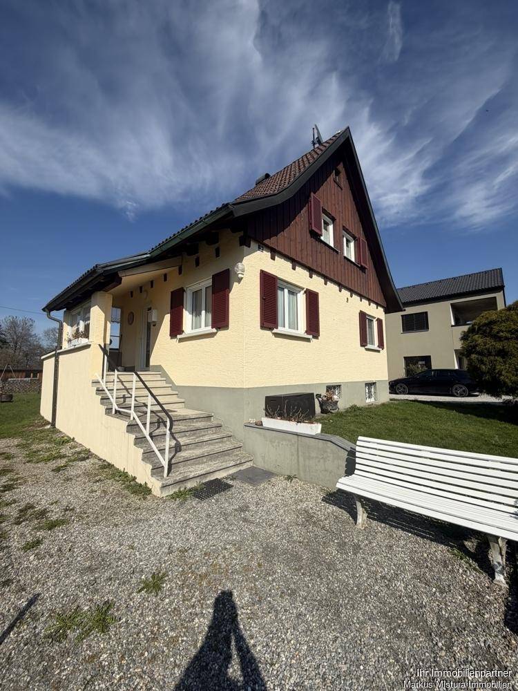 Ansicht des Einfamilienhauses von der Zufahrt aus mit Außentreppe und Gartenbank.