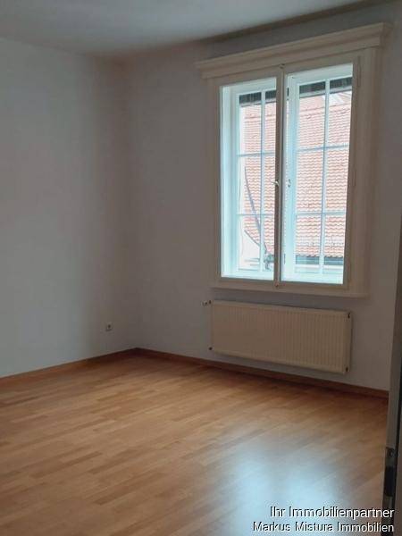 Helles Zimmer mit Parkettboden und großem Fenster, das viel Tageslicht hereinlässt.