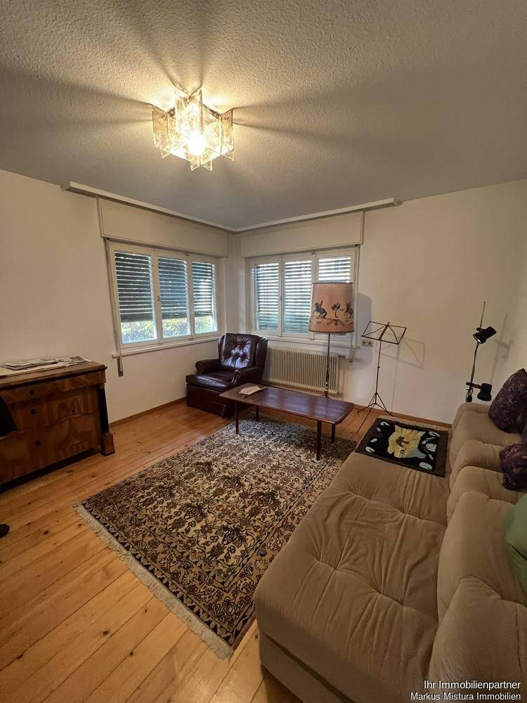 Gemütliches Wohnzimmer mit Holzboden, Sofa, Sessel und einem Teppich.