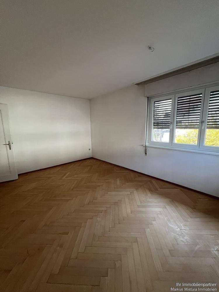 Geräumiges Zimmer mit klassischem Fischgrätparkettboden und Fenster mit Außenjalousien.