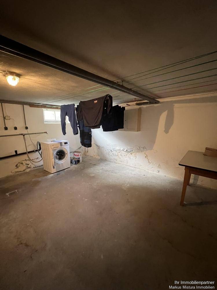 Waschküche im Keller mit Waschmaschine, Wäscheleinen und einfacher Ausstattung.