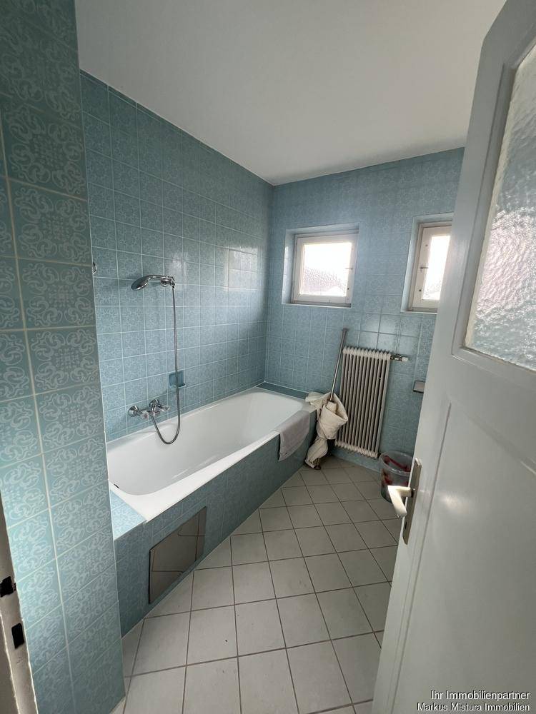 Badezimmer mit hellblauen Fliesen, Badewanne und zwei kleinen Fenstern, typisch für die 80er Jahre.