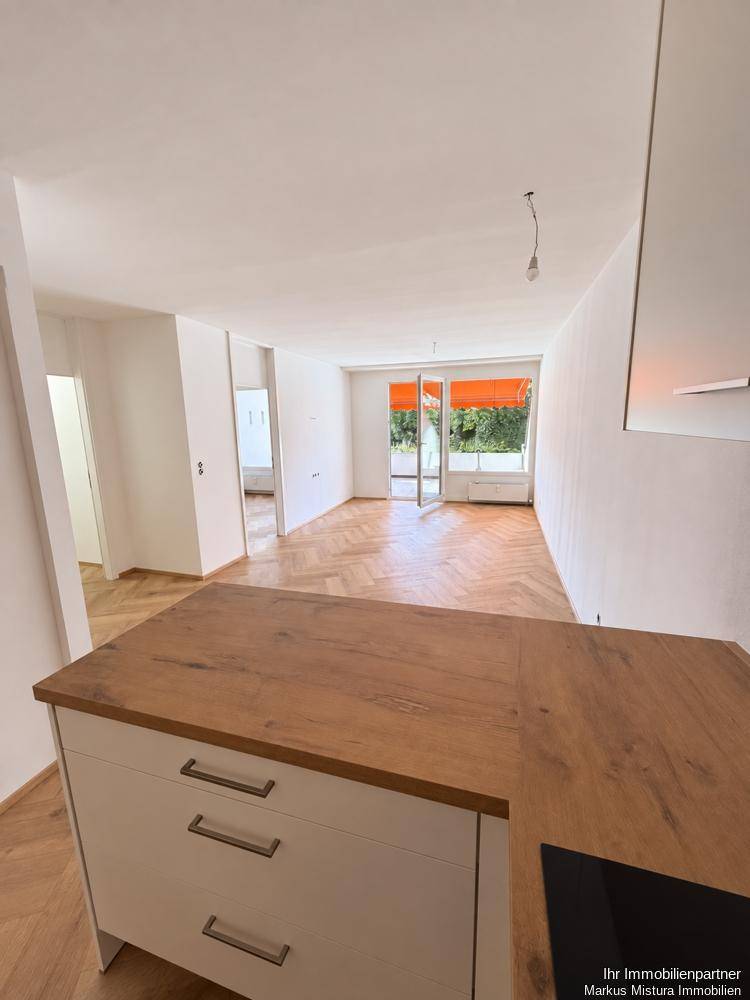 Blick von der Küche in den hellen Wohnbereich mit Fischgrätparkett und Terrassenzugang.