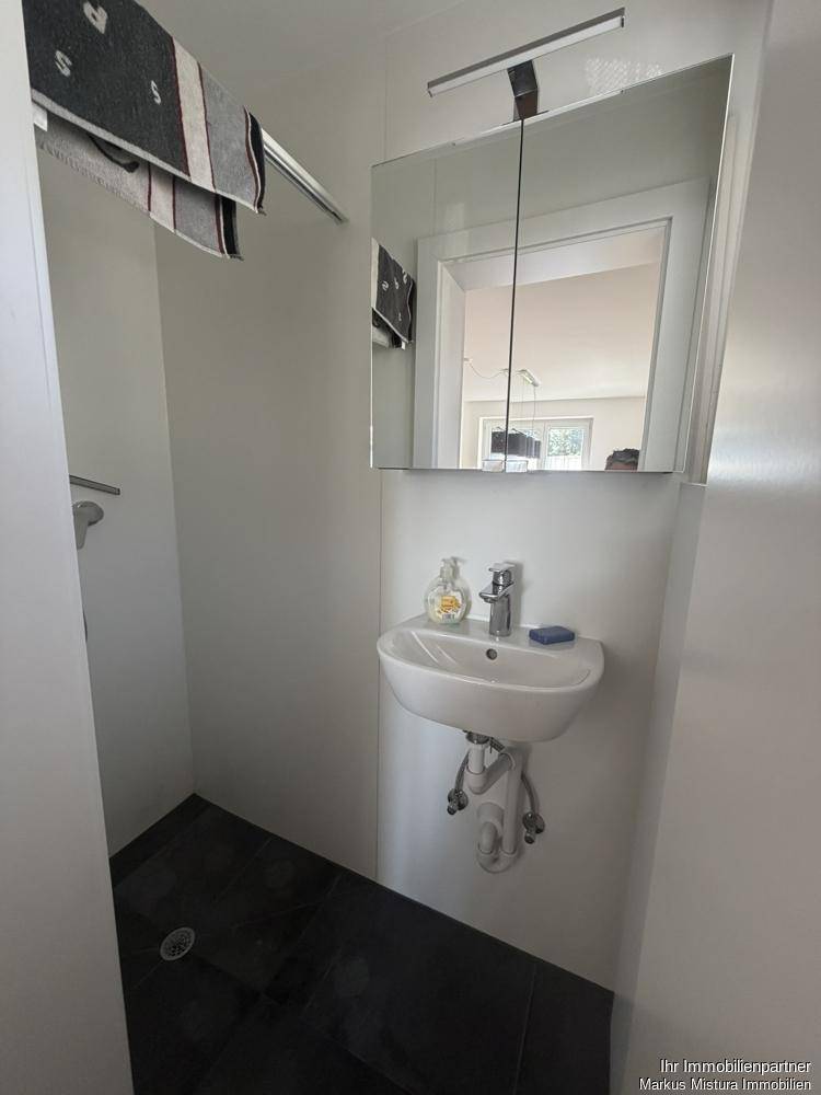 Kleines, modernes Badezimmer mit Waschbecken, Spiegelschrank und dunklen Fliesen.