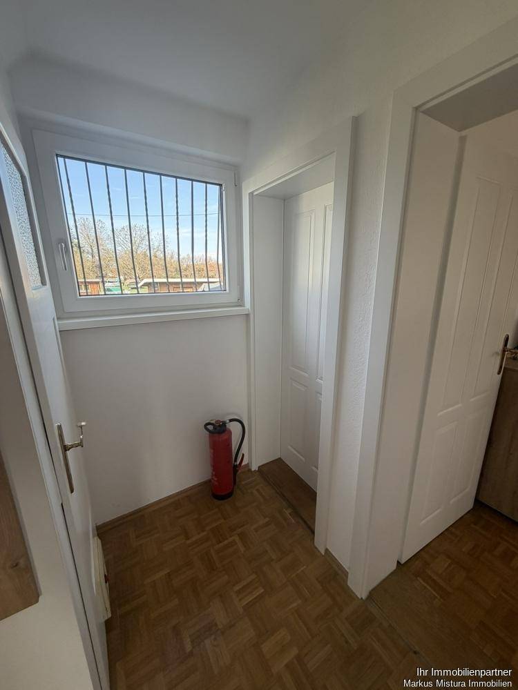 Flur mit Fenster und Parkettboden, der Zugang zu weiteren Räumen bietet.