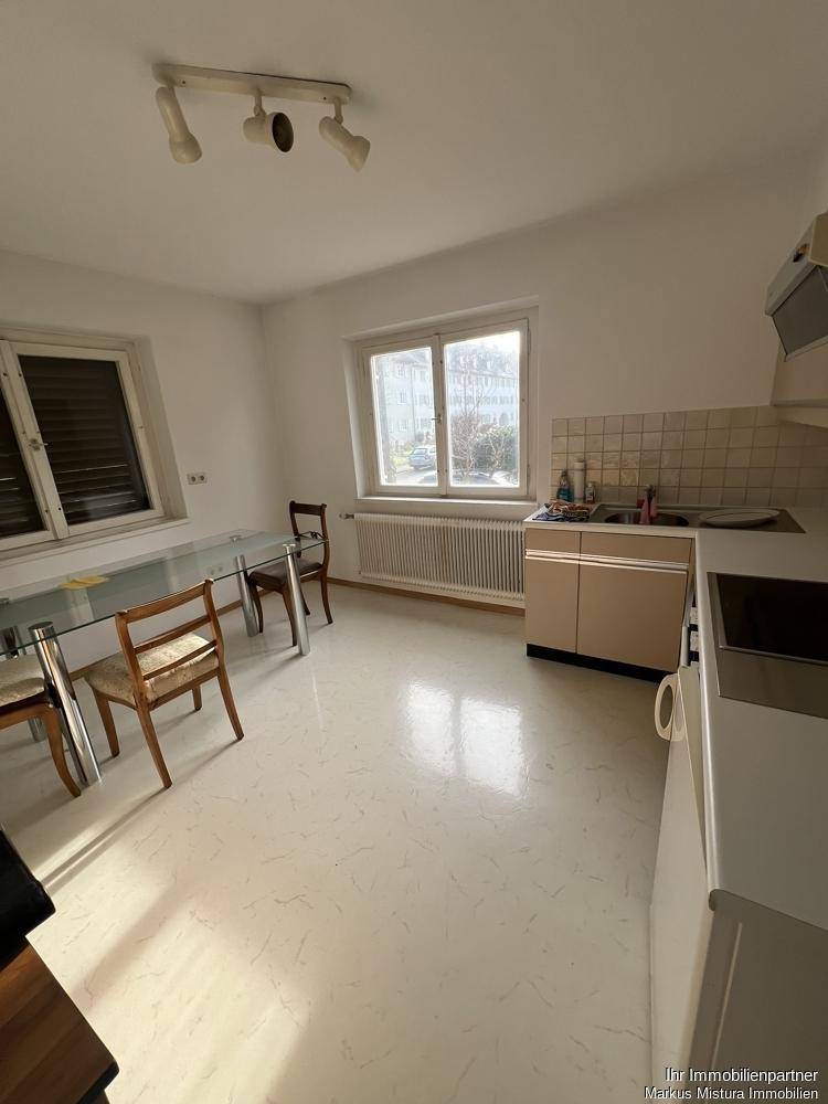 Helle Küche mit älterer Einbauküche, Essbereich und Fenster mit Blick nach draußen.