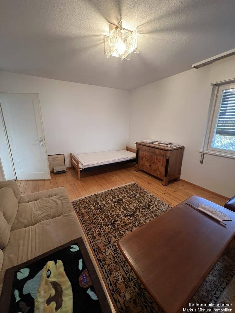 Helles Schlafzimmer mit Holzboden, Bett, Kommode und Fenster mit Jalousien.