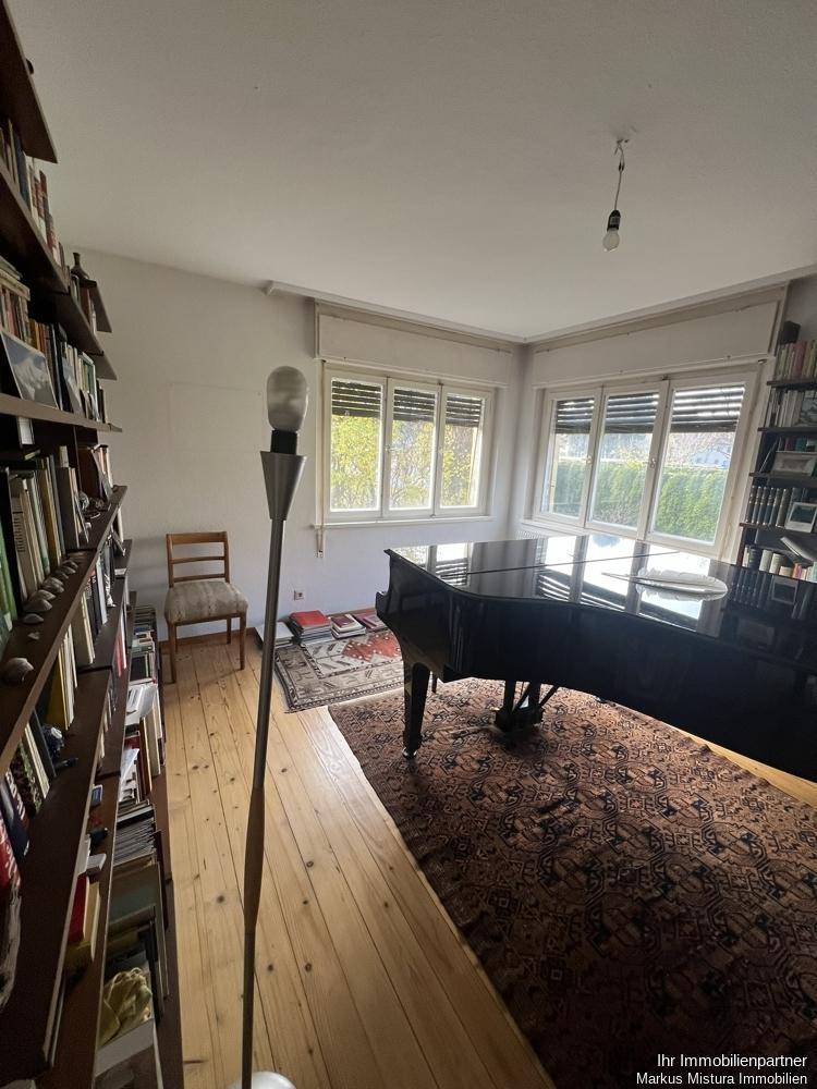 Geräumiges Wohnzimmer mit Holzfußboden, Bücherregalen und einem Flügel am Fenster.