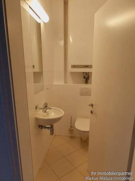 Kleines, hell gefliestes Gäste-WC mit Waschbecken, Toilette und Spiegelschrank.