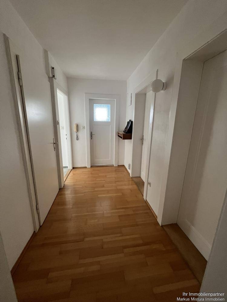 Heller Flur mit Holzparkettboden und weiß gestrichenen Wänden, der zu mehreren Räumen führt.