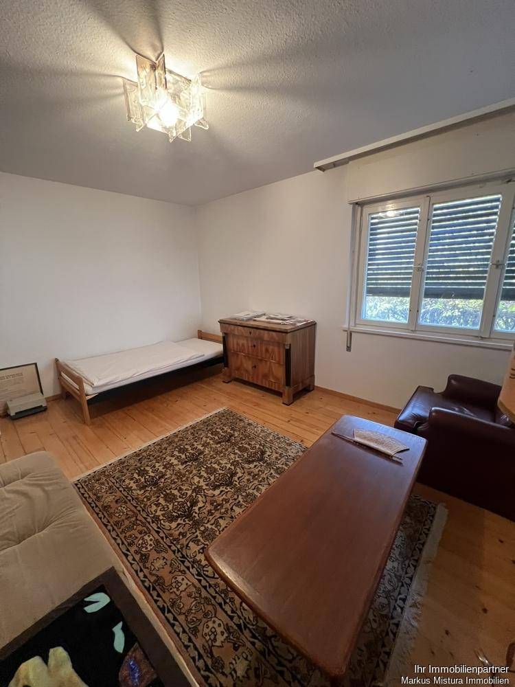 Schlafzimmer mit Holzboden, Einzelbett, Kommode und einem Teppich.