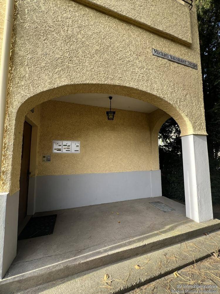 Überdachter Eingangsbereich mit Bogenarchitektur, Briefkästen und einer Straßenbezeichnung.