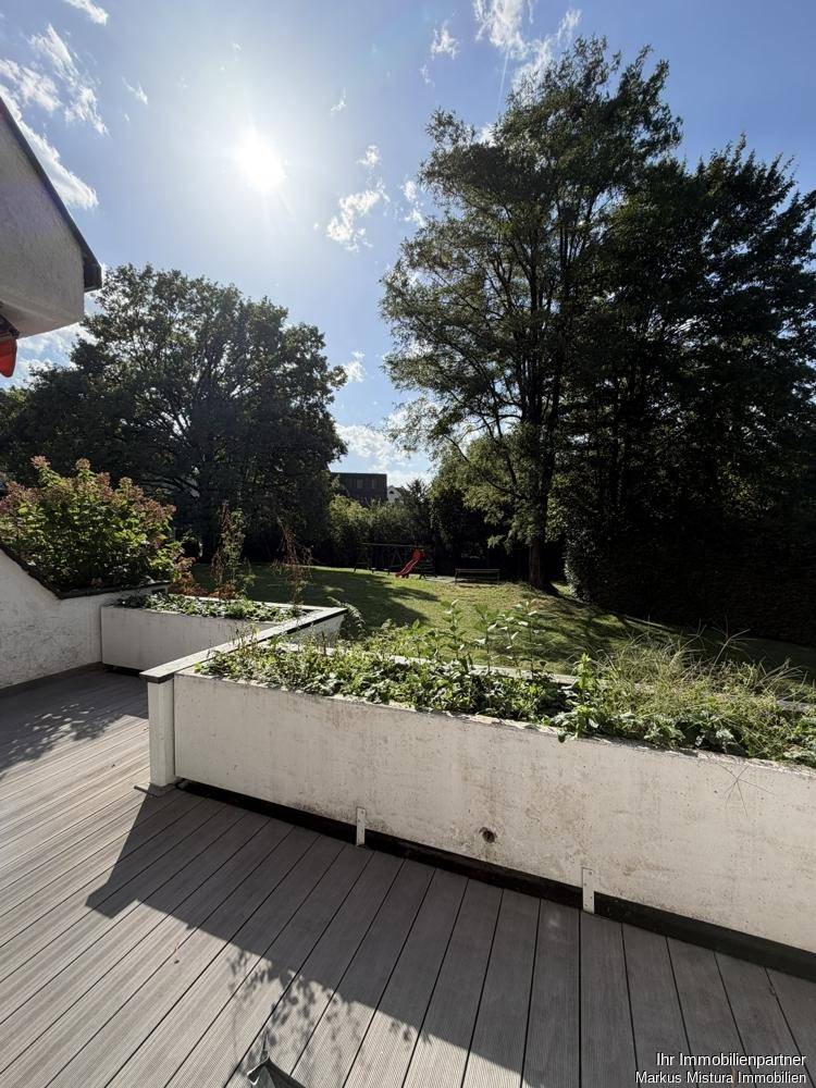Sonnige Terrasse mit Holzbelag und weitem Blick auf den großen Gemeinschaftsgarten.