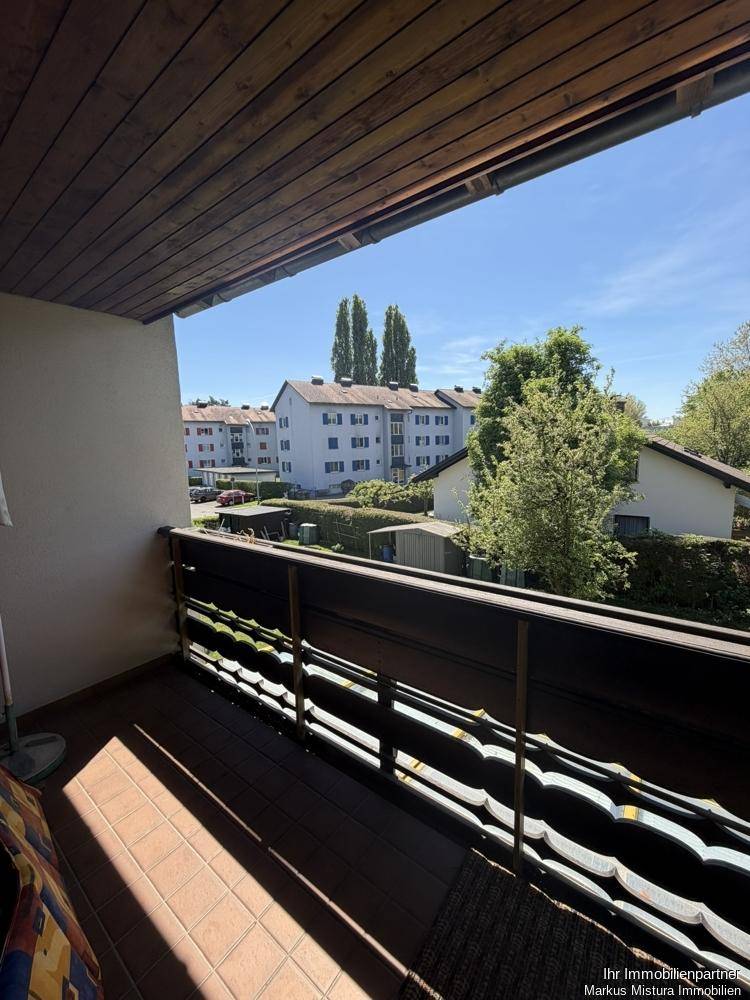 Balkon mit Fliesenboden und Blick auf die umliegenden Gebäude und Bäume.