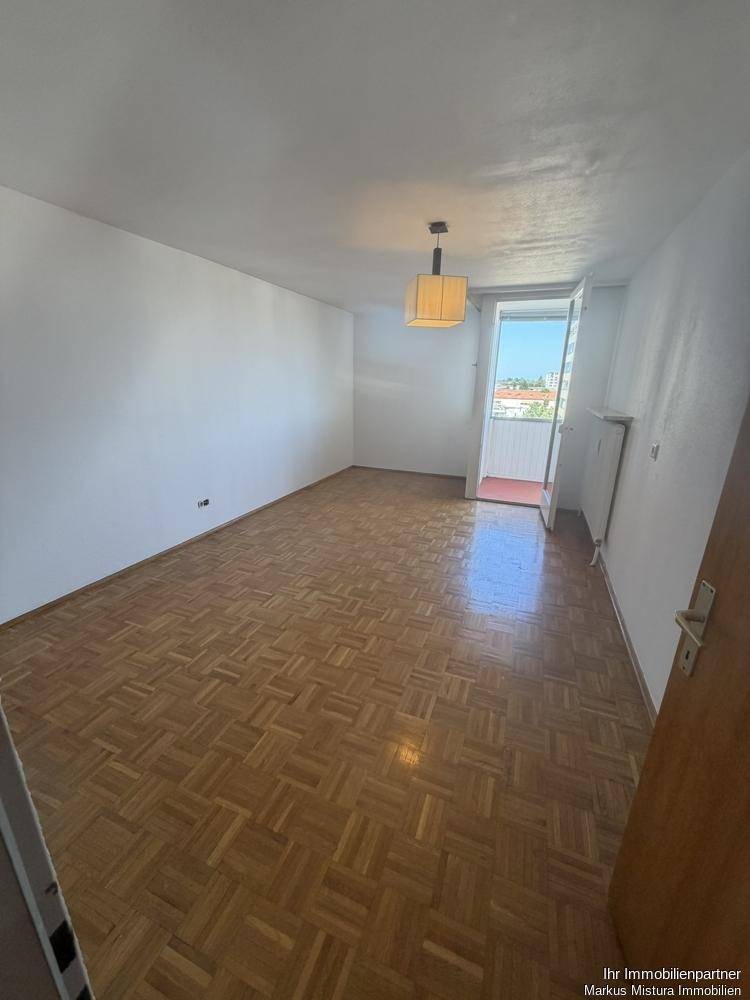 Helles Zimmer mit Parkettboden und Zugang zu einem kleinen Balkon.
