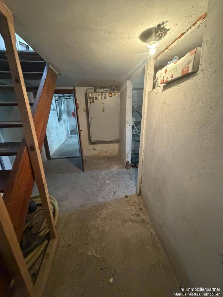 Unausgebauter Kellerraum mit Betonboden und sichtbaren Installationen, der als Lager dient.