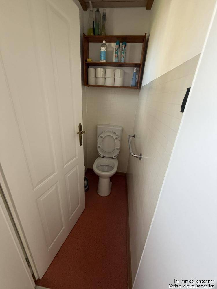 Separate Toilette mit WC, kleinem Regal und roten Bodenfliesen.