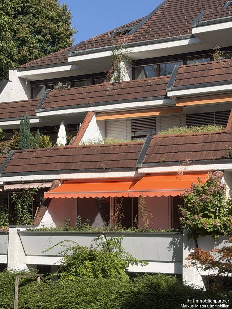 Fassade eines Wohngebäudes mit mehreren Terrassen, roten Markisen und begrünten Dächern.
