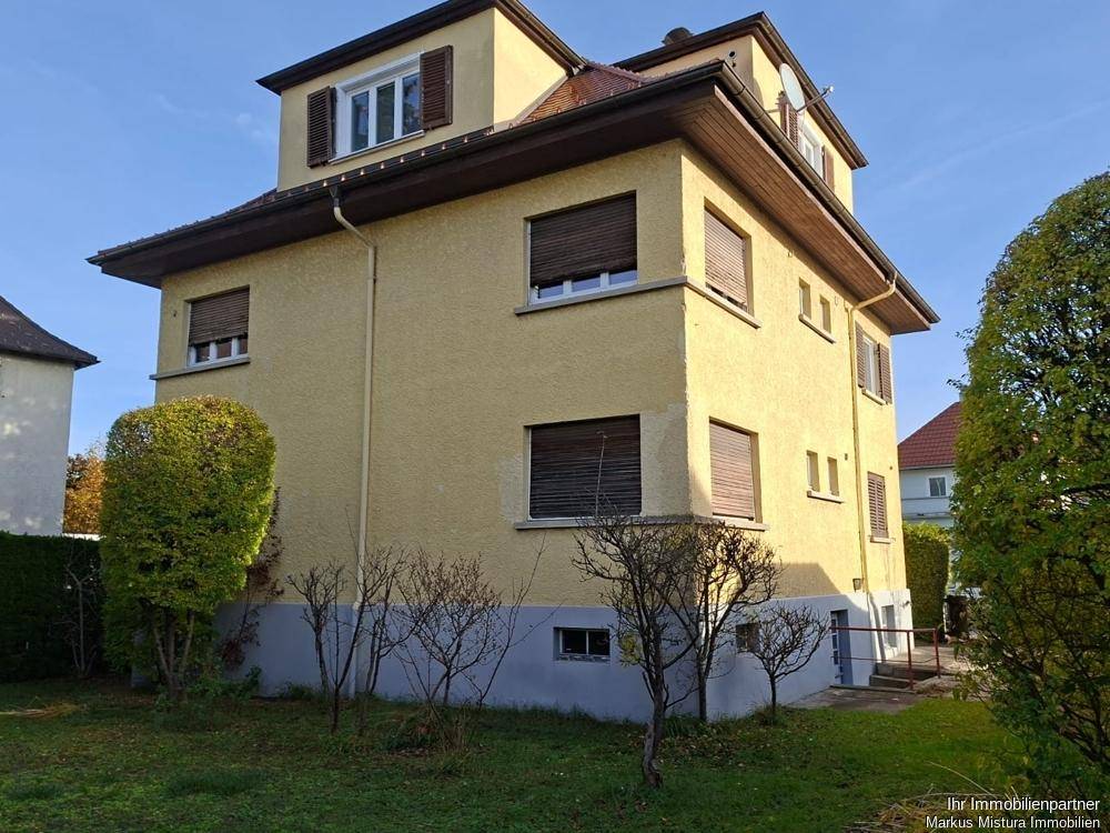 Seitenansicht des gelben Mehrfamilienhauses mit Gartenbereich und kleinen Bäumen.