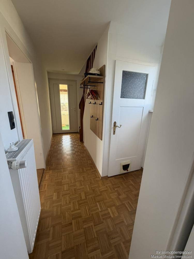 Heller Flur mit Parkettboden und Garderobe, der zu verschiedenen Zimmern führt.