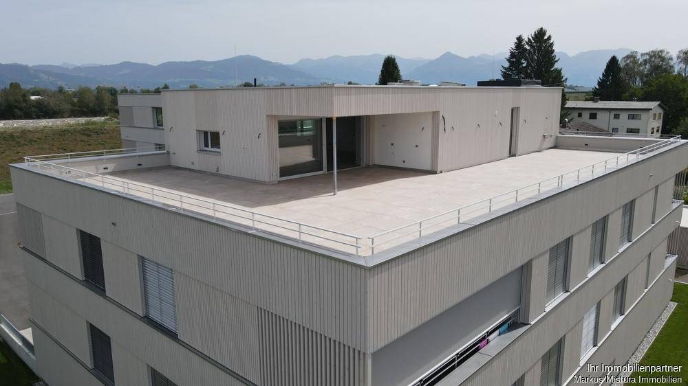 Moderne Architektur des Wohngebäudes mit großer Dachterrasse und Bergblick im Hintergrund.