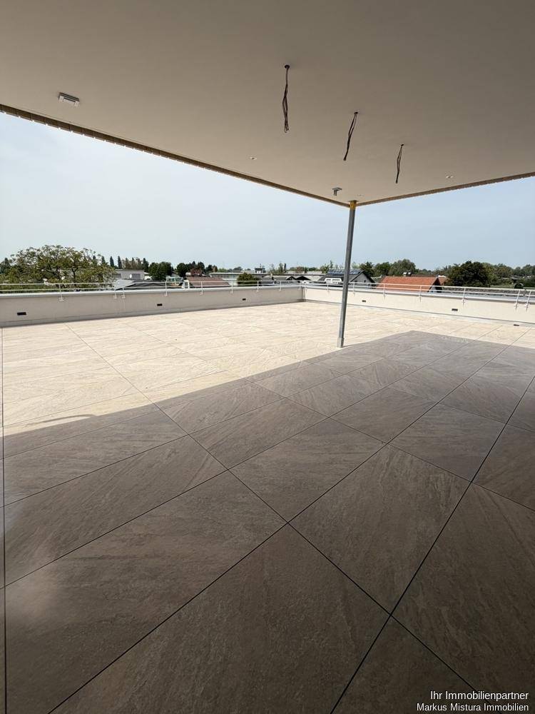 Überdachter Bereich der Dachterrasse mit Fliesenboden und weitem Ausblick auf die Umgebung.