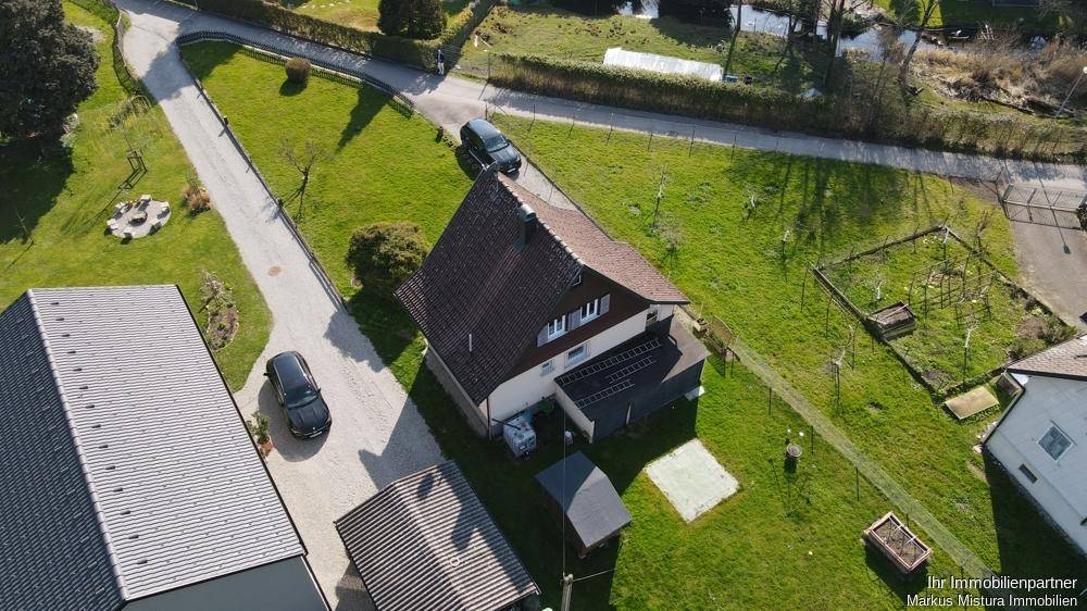 Luftaufnahme eines Einfamilienhauses mit weitläufigem Grundstück und angrenzendem Wasserlauf.