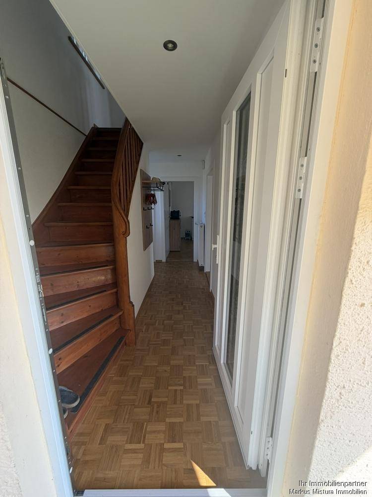Heller Eingangsbereich mit Holztreppe und Parkettboden, der zu weiteren Räumen führt.