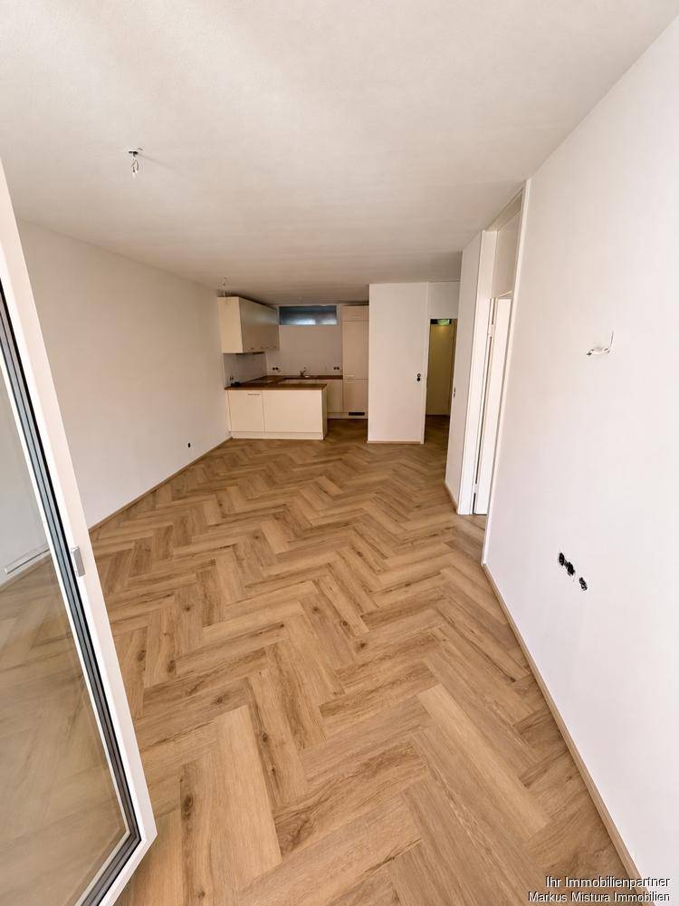 Offener Wohnbereich mit Fischgrätparkett und Blick auf die neue, ungenutzte Küche.