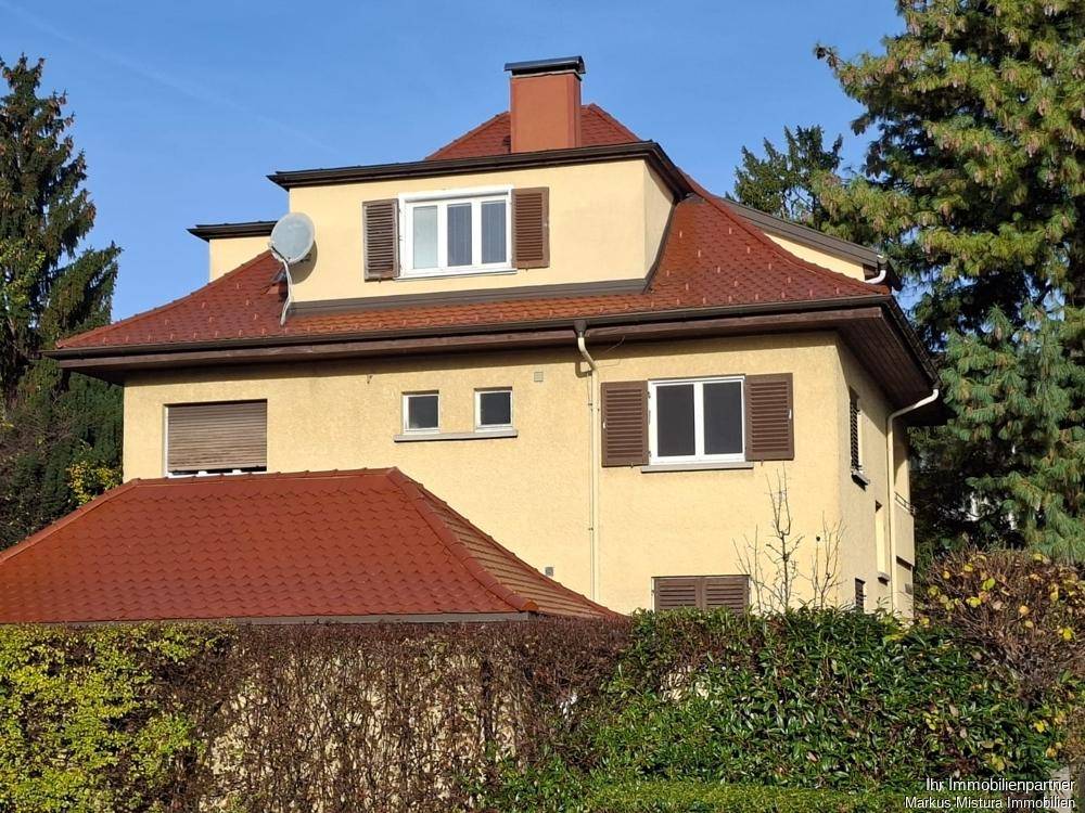 Vorderansicht eines gelben Hauses mit rotem Ziegeldach, Schornstein und Satellitenschüssel.