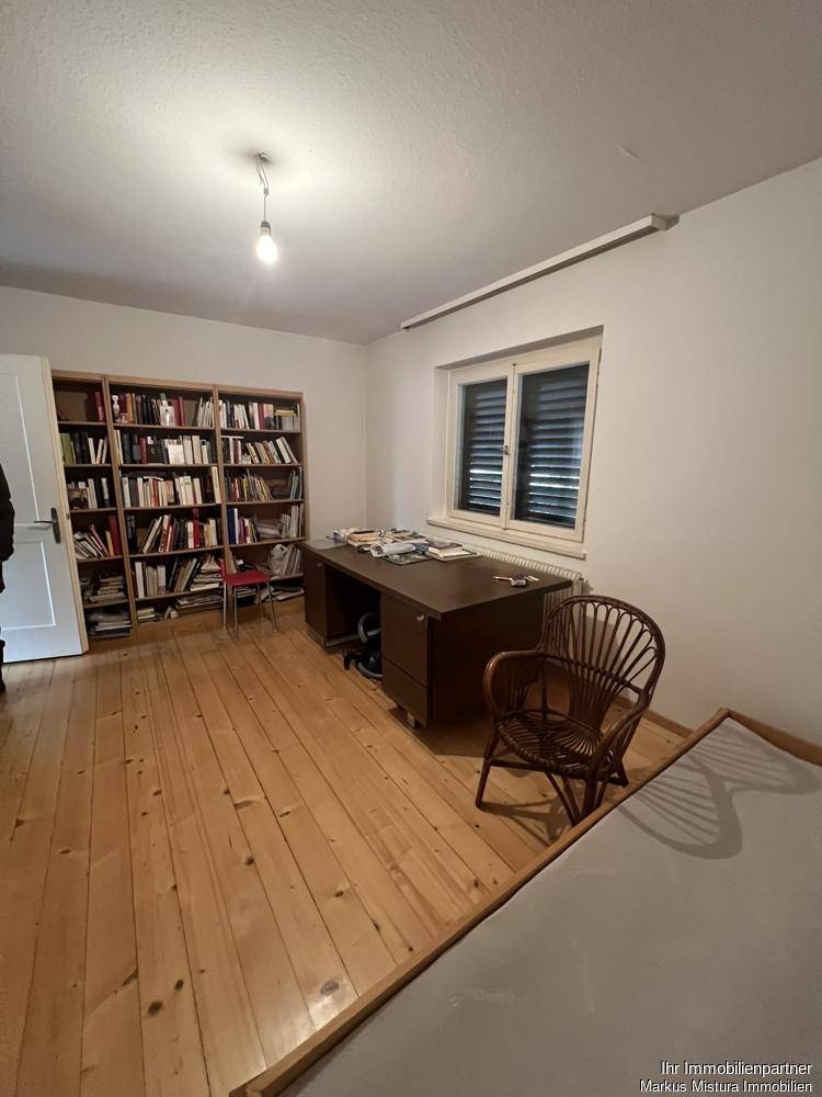 Arbeitszimmer mit Holzboden, großem Schreibtisch und Bücherregalen entlang der Wand.