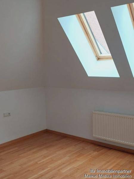 Dachgeschosszimmer mit schrägen Wänden, Parkettboden und zwei Dachfenstern für viel Licht.