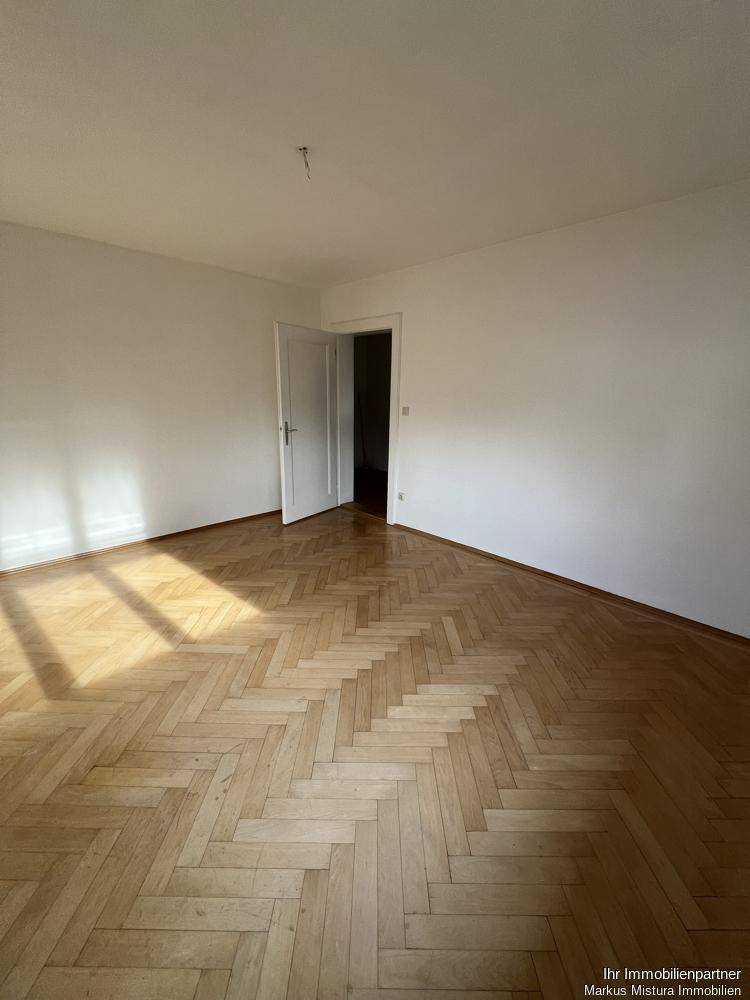 Geräumiges Zimmer mit Fischgrätparkett und viel Tageslicht, bereit zur Einrichtung.