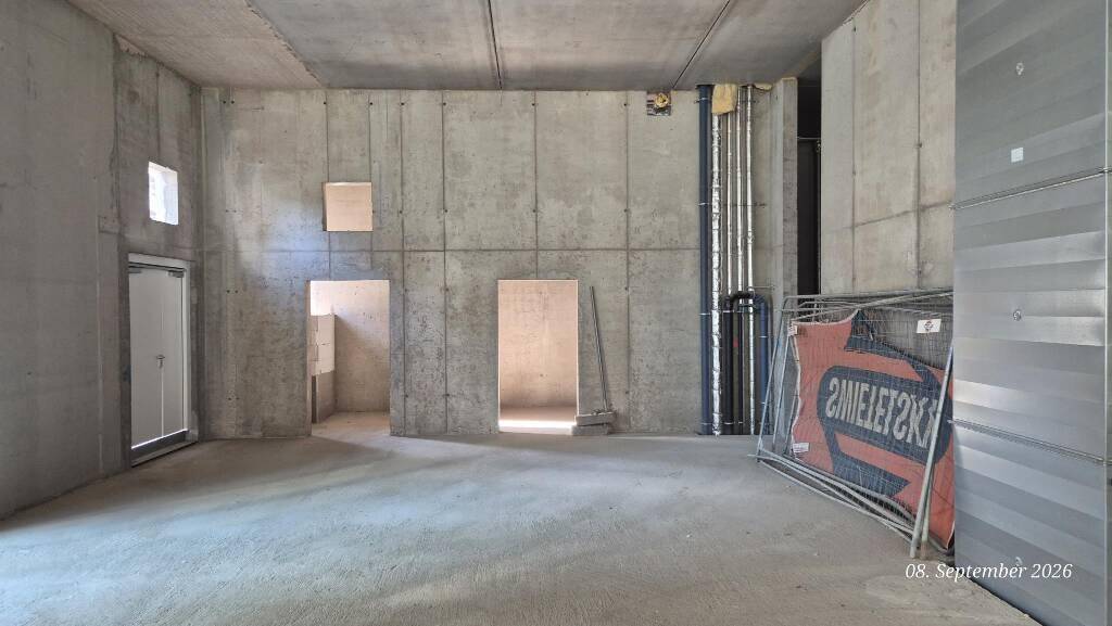 Rohbau-Innenraum mit Betonwänden, mehreren Türöffnungen und einem kleinen Fenster, noch unfertig.