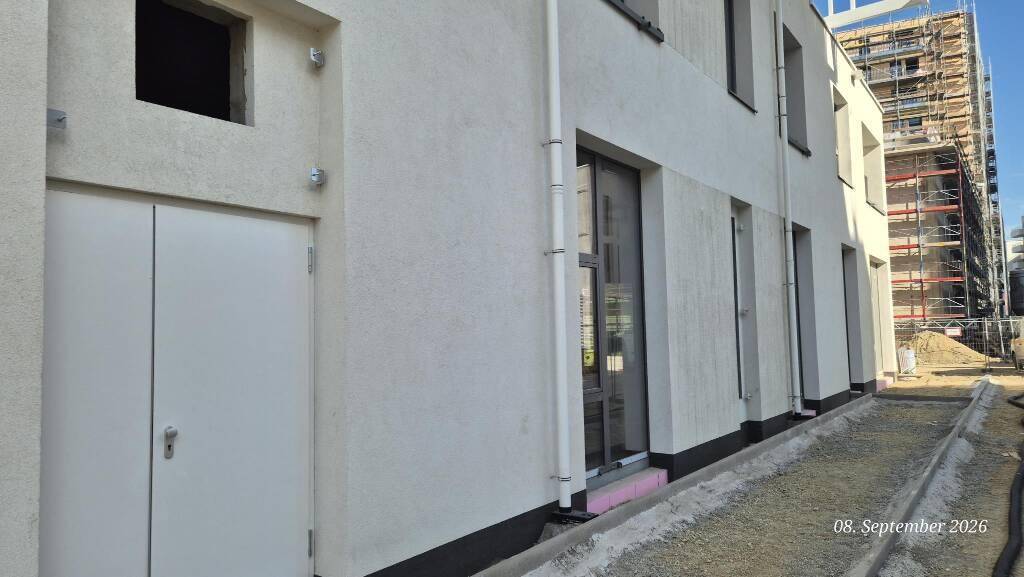 Außenansicht des Erdgeschosses eines Neubaus mit weißer Fassade, Eingangstür und Baustellenbereich.