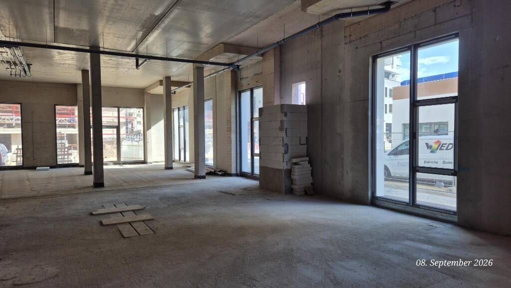 Weitläufiger Rohbau eines Gewerberaums mit Betonböden, Säulen und großen Fensterfronten.
