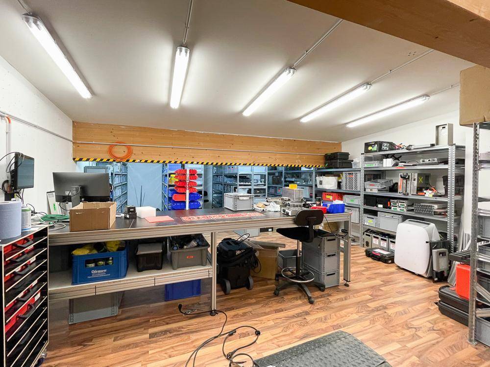 Funktionaler Arbeitsbereich mit Holzfußboden, Regalen und guter Beleuchtung durch Deckenleuchten.