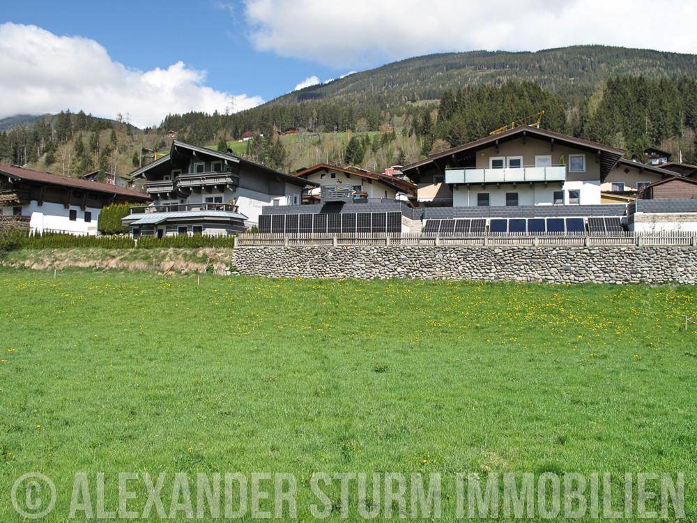 Reihe von Wohnhäusern mit Balkonen und Solaranlagen vor einer bewaldeten Bergkulisse.