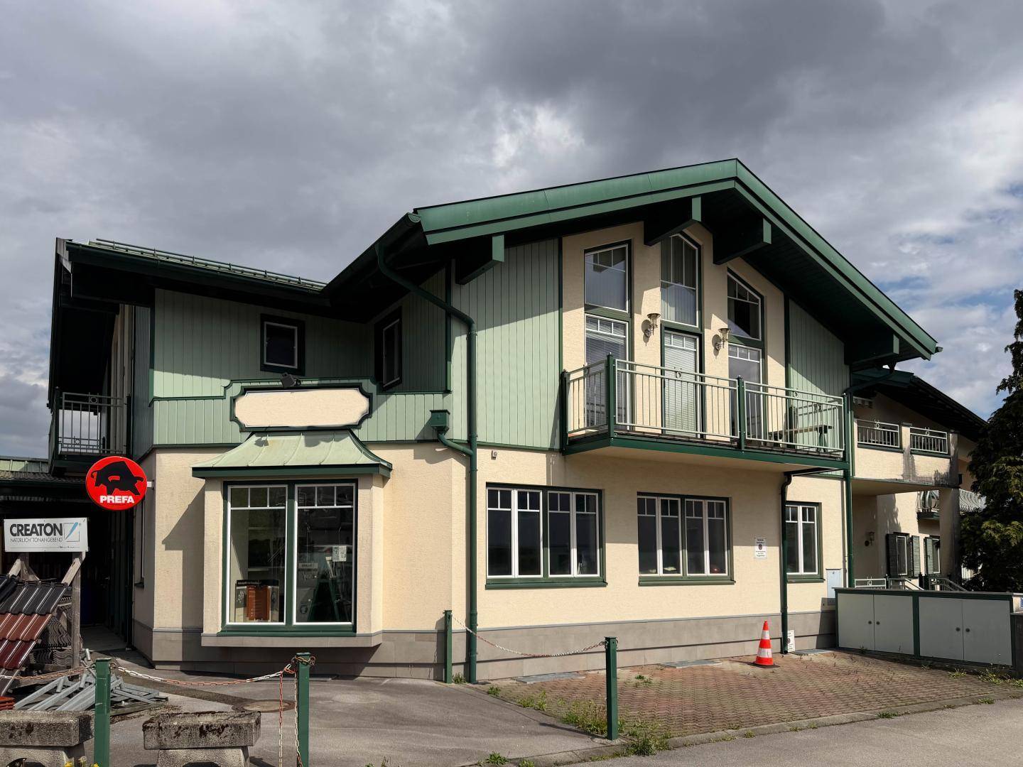 Attraktives Gebäude mit grünen Dachelementen, hellen Fassaden und mehreren Balkonen unter bewölktem Himmel.