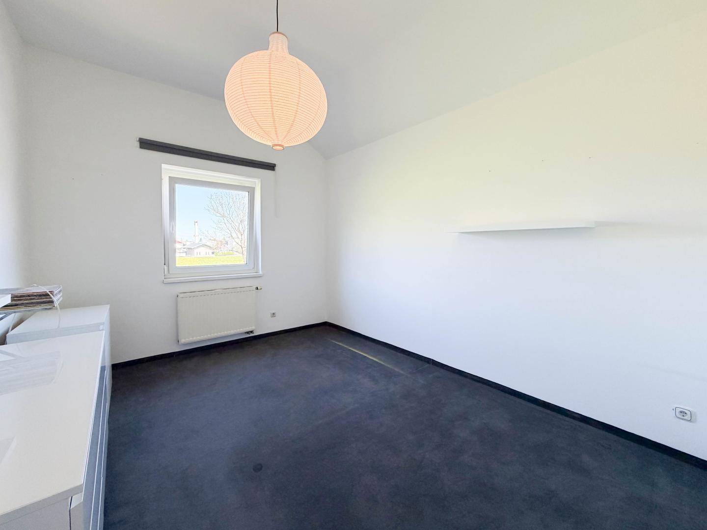 Helles Zimmer mit weiß gestrichenen Wänden, Teppichboden und einem Fenster mit Ausblick.